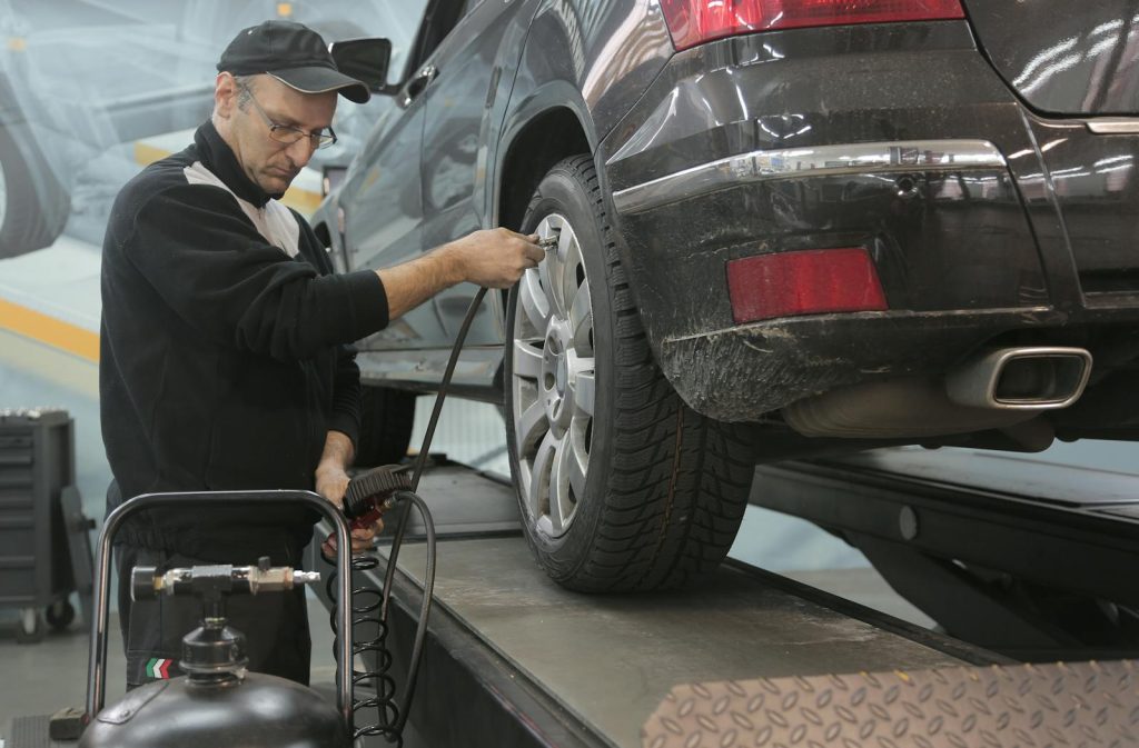 Serious car mechanic pumping up car wheel in modern service garage